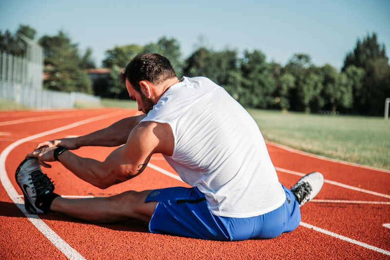 Man stretching his hamstrings on a running track before training